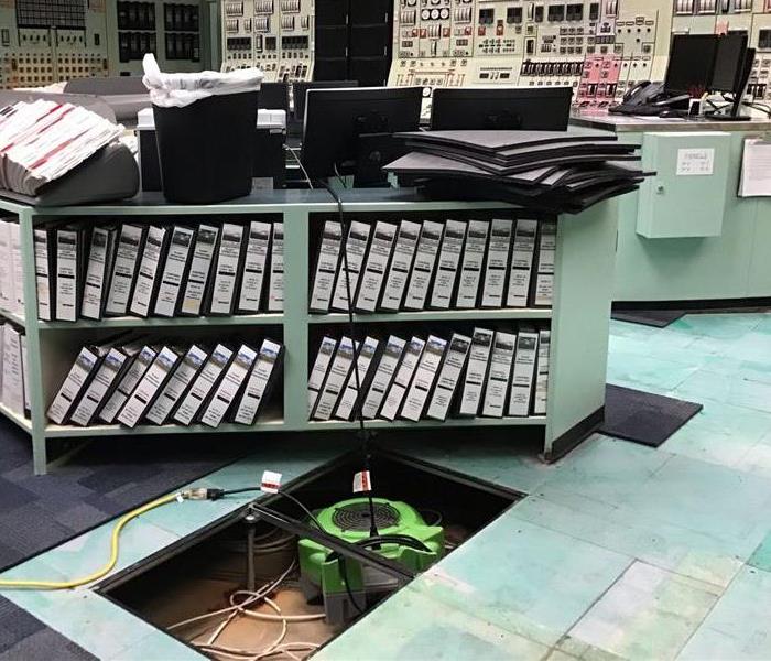 office room with many books and control panels with fan drying inside the floor