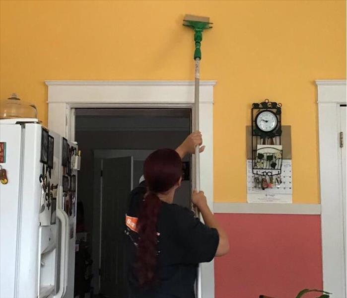 female SERVPRO employee using long brush to wipe down orange wall in kitchen